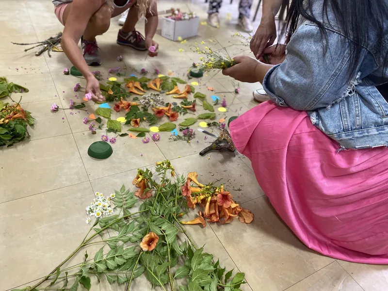 Adultos e crianças a construir uma mandala de flores no chão, no Educar Fora da Sala de Aula